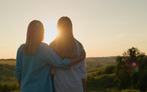 Due figure femminili prese di spalle che guardano il sole mentre si abbracciano