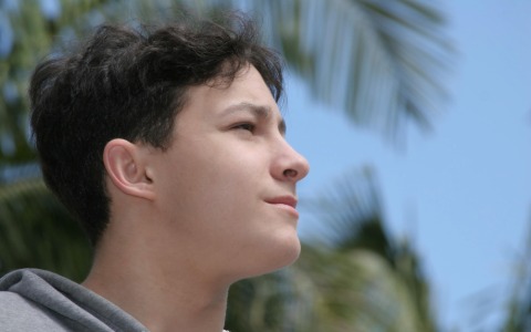 volto di un giovane ragazzo dai lineamenti caucasici e con capelli lisci neri. sta guardando qualcosa davanti a lui